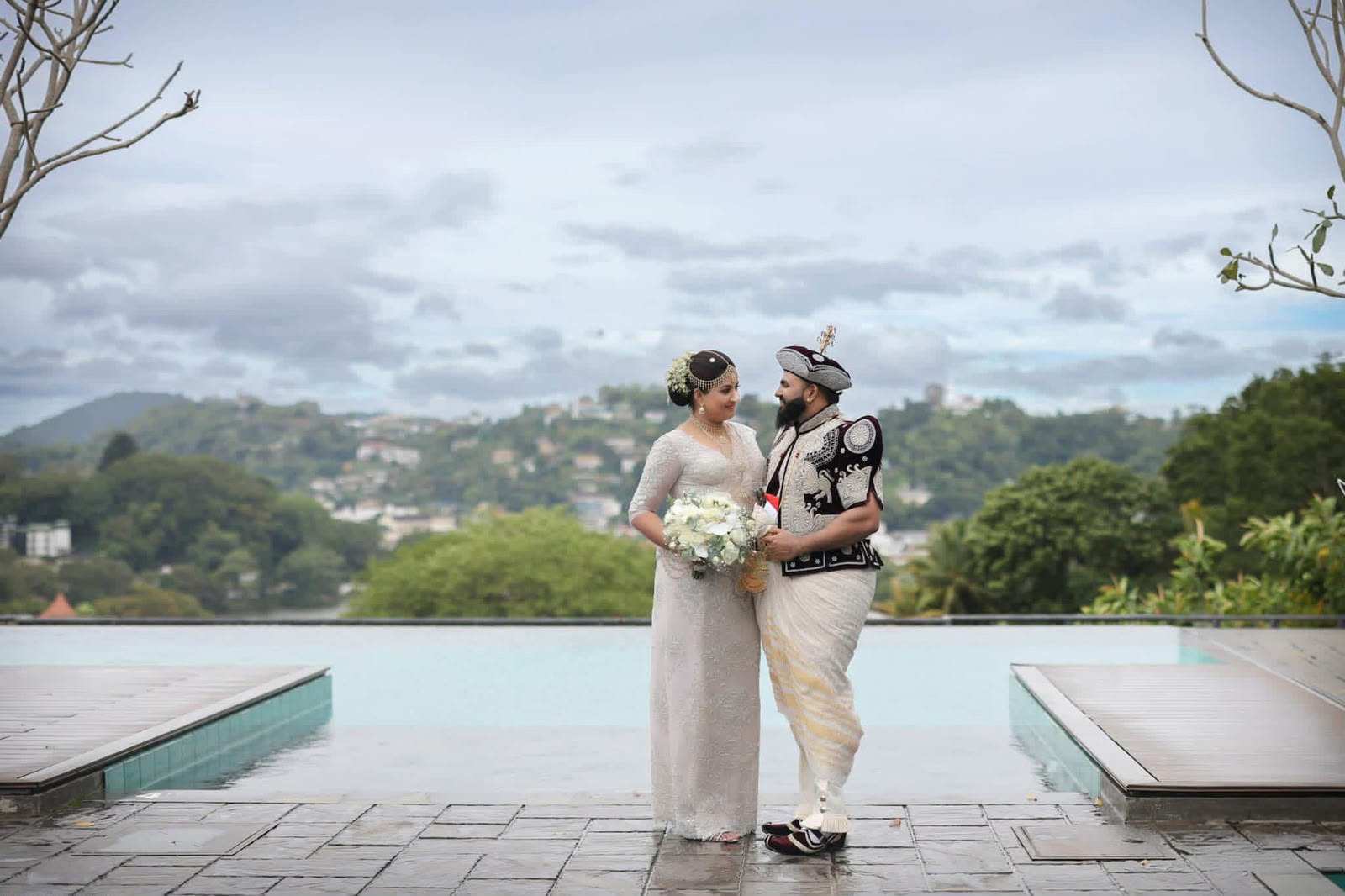 A couple in traditional Kandyan wedding attire beside an infinity pool overlooking the Kandy hills